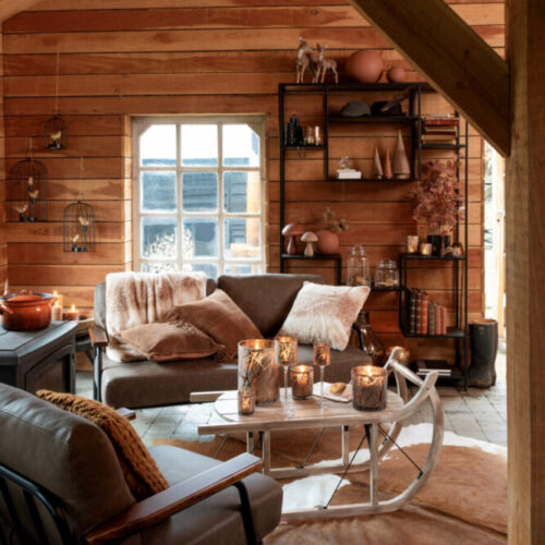 étagère 10 planches en bois de manguier et fer de couleurs brun foncé et noir dans un salon chaleureux avec canapé gris table basse forme luge en bois blanc et fauteuil lounge gris vu de dos avec tapis peau de vache blanc et marron
