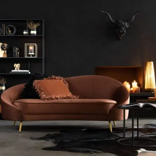 sofa en velours marron et pieds en métal or dans un salon au mur noir avec un tapis noir une étagère en métal sur l'arrière du canapé comportant plusieurs bibelots et sur la droite un cadre représentant une tête de cheval marron