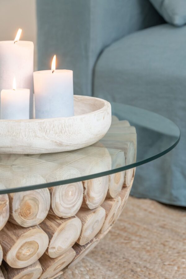 table basse ronde en teck naturel avec plateau en verre sur un tapis beige avec des bougies blanches posées dessus