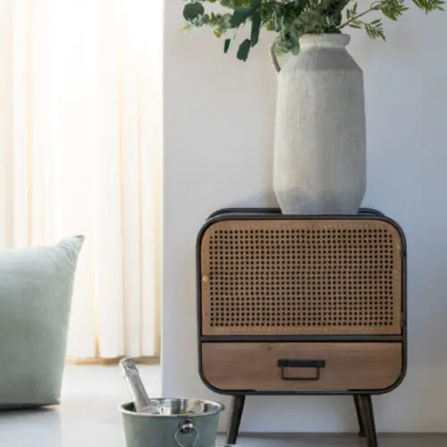 Table de chevet table de chevet avec cadre en métal noir et porte et tiroir en bois naturel sur pieds en métal noir avec un vase gris et des fleurs avec devant une table avec une tasse mug posé dessus
