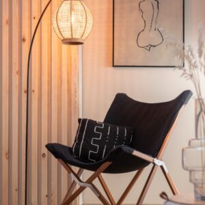 coussin en coton noir avec graphiques lignes beiges sur un fauteuil lounge en tissu noir et pieds en bois avec lampadaire en métal couleur or