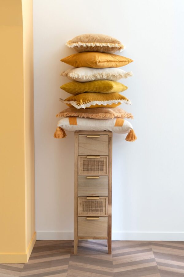 petite armoire fine en bois et rotin naturel tas de coussins posés dessus dans les teintes ocre orangées