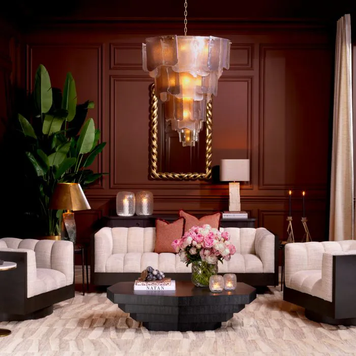 Canapé Davide Eichholtz capitonné crème sur socle noir, dans un salon boisé éclairé par un lustre — mobilier de luxe chez Melimel Home
